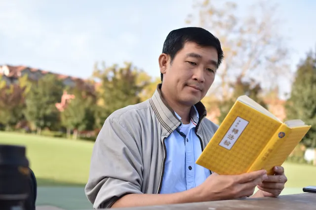 Мъж чете книгата на Фалун Дафа, "Джуан Фалун" на китайски език. Мъж азиатец чете навън из зеленина книгата на Фалун Дафа на китайски език.