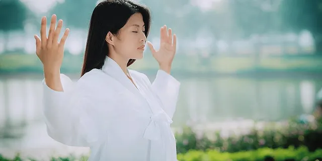 Жена прави упражненията на Фалун Дафа. Азиатка в бяла роба прави стоящо упражнение на Фалун Дафа навън.