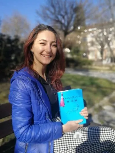 Момиче държи "Джуан Фалун", основната книга на Фалун Дафа. Момиче е седнало на пейка, усмихва се и държи "Джуан Фалун", основната книга на Фалун Дафа.